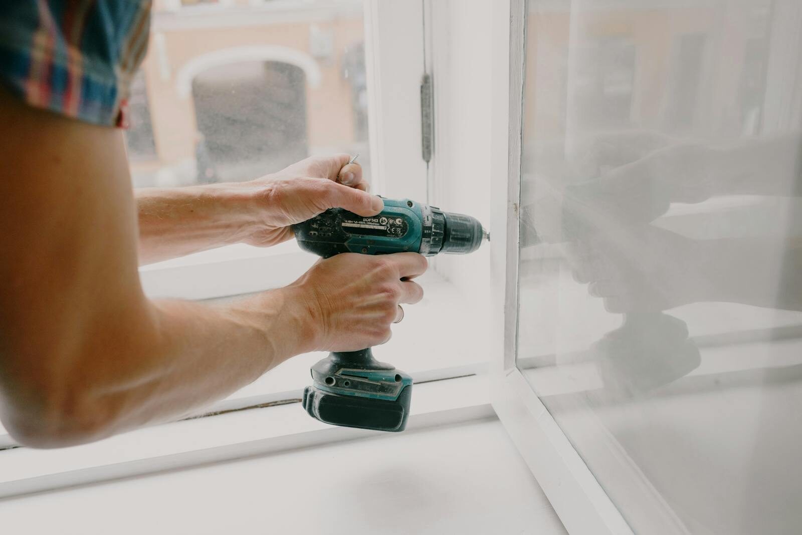 Photo by Ksenia Chernaya Side view of crop anonymous male mechanic fixing window with screwdriver during renovation process in apartment